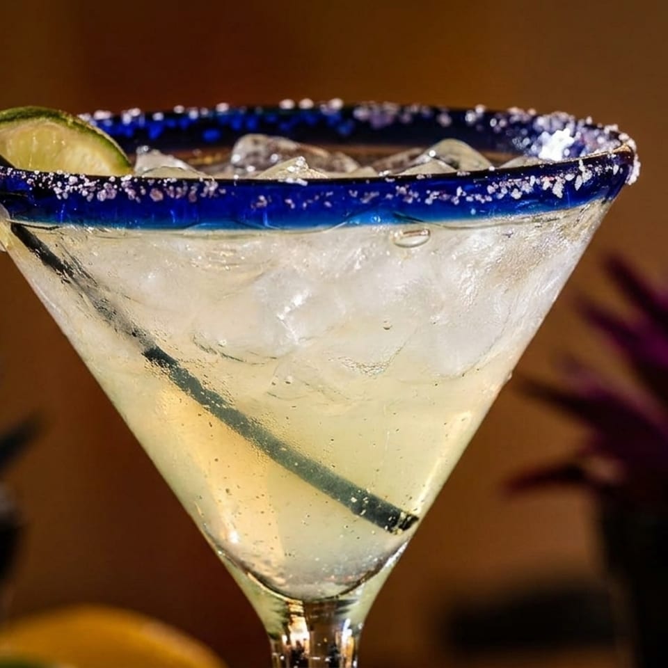 Close-up of a margarita in a salt-rimmed glass with a lime wedge and straw.