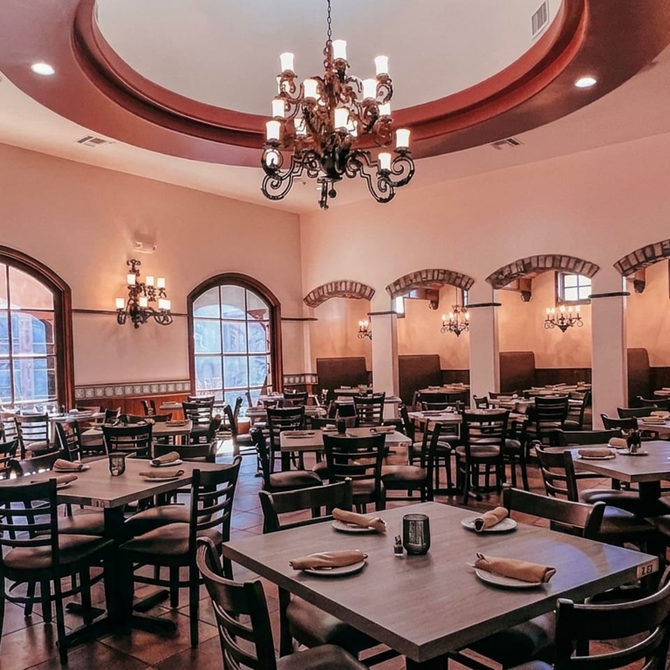 Spacious restaurant dining room with many tables, arched windows, and decorative chandeliers.