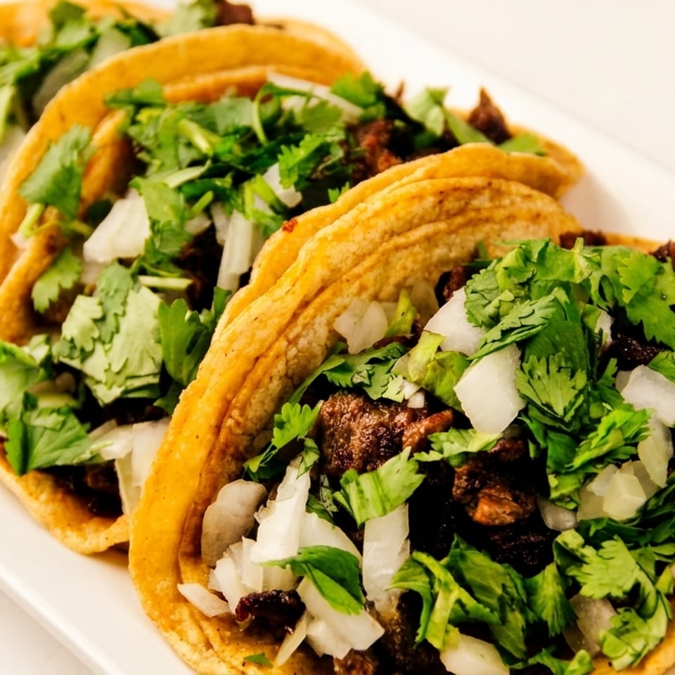 Three delicious street tacos filled with carne asada, diced onions, and fresh cilantro.