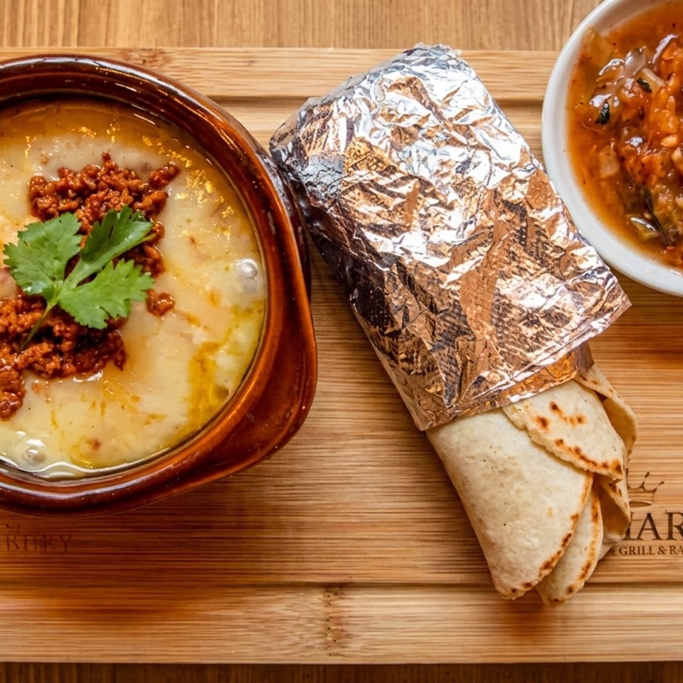A bowl of queso fundido with chorizo, a foil-wrapped burrito, and a side of salsa on a wooden board.